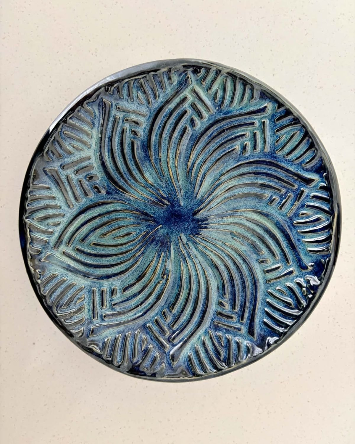 Round plate carved with a swirling flower pattern under a pale blue glaze