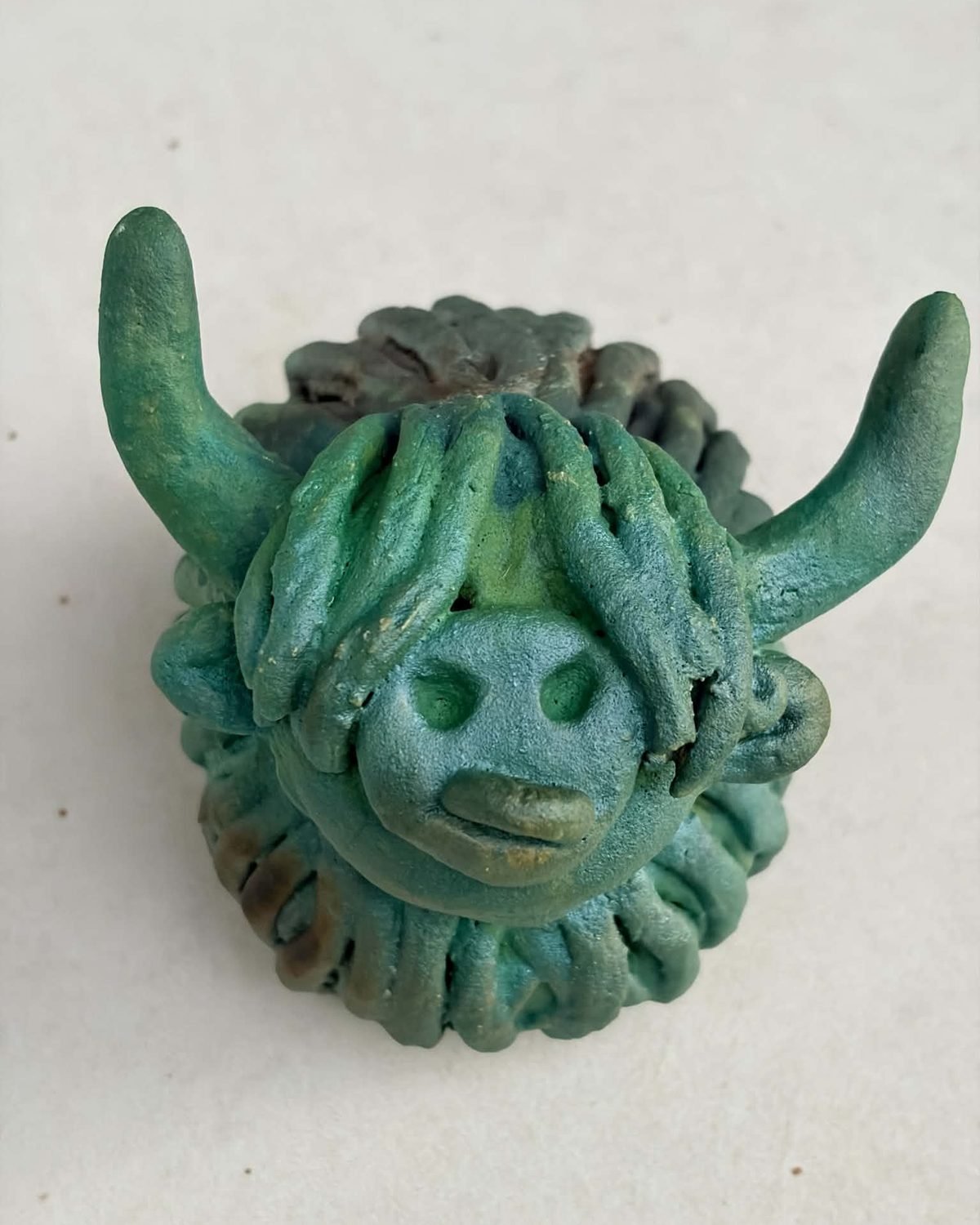 Hamish, a handmade ceramic Highland cow with a green glaze with a heavy fringe and a downturned mouth