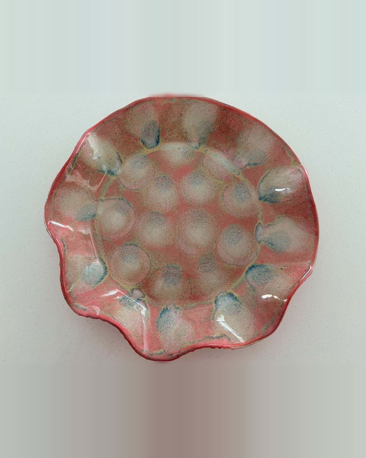 Shallow ruffled bowl in coral pink with pale dimples