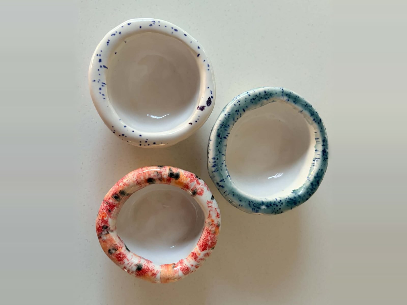 Three small handmade pinch bowls with speckled white, blue and coral rims